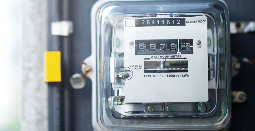 Les mains d'un technicien tiennent un multimètre devant un compteur électrique résidentiel